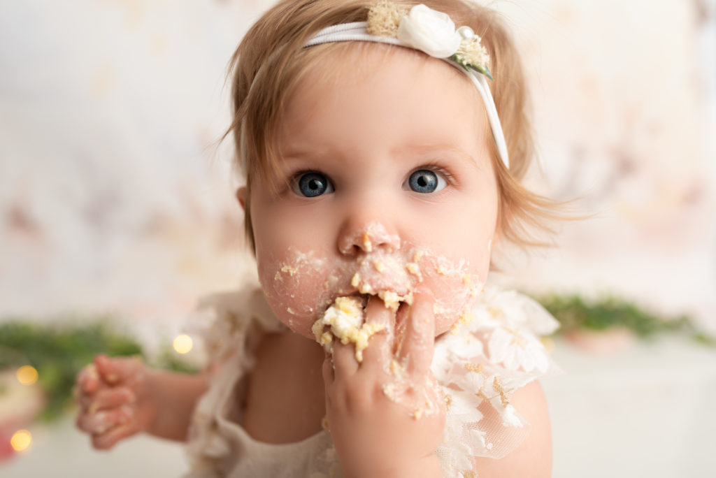 One year old girl with cake all over her face at her one year cake smash session in charlotte