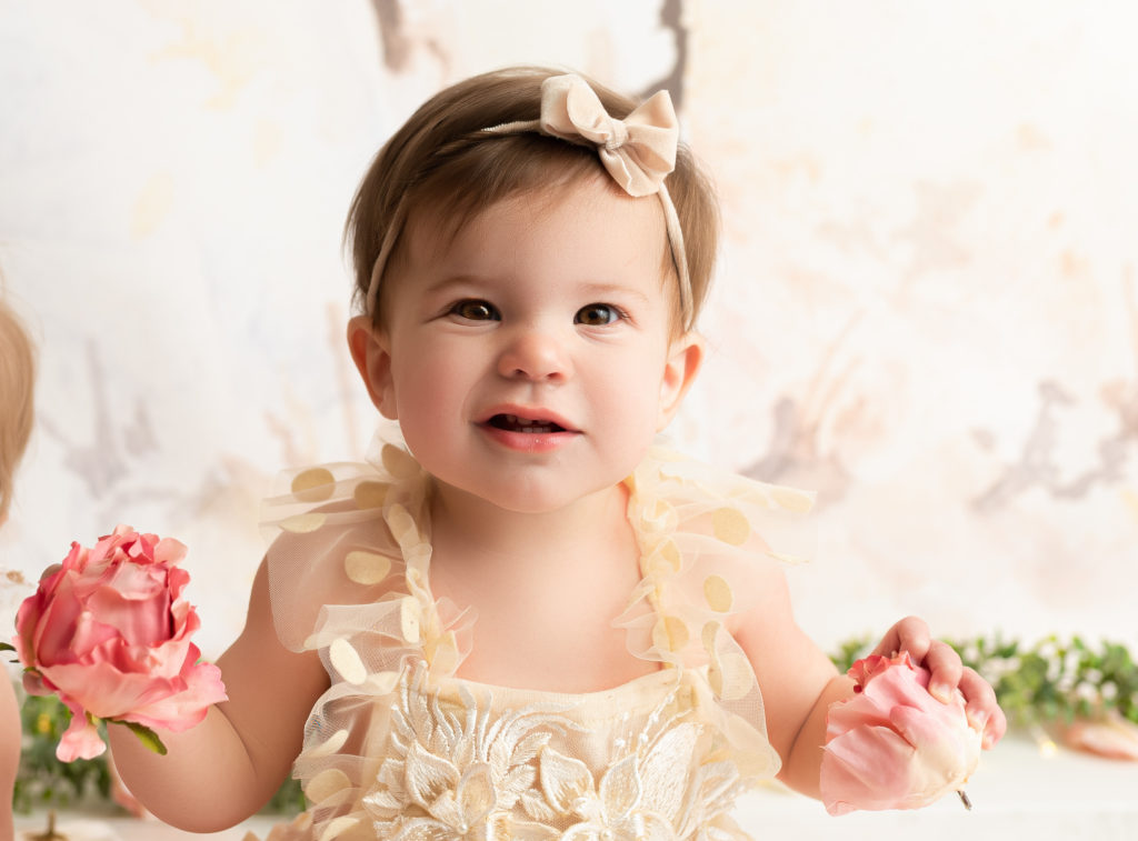 One year old girl holding flowers with a smirk during her cake smash session