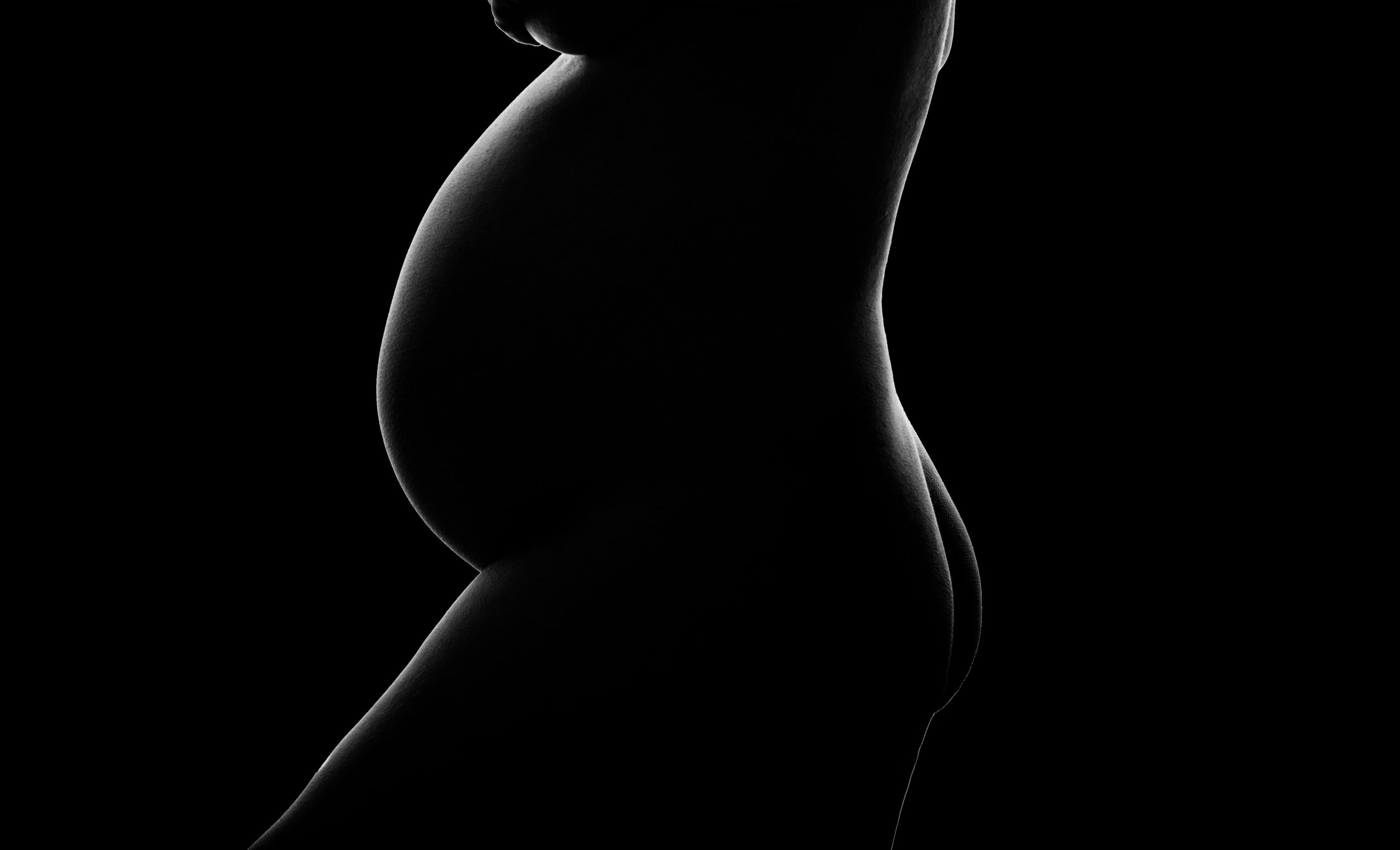Black and white photo silhouette of pregnant mother showing off her bump and curves at a charlotte maternity photography studio.