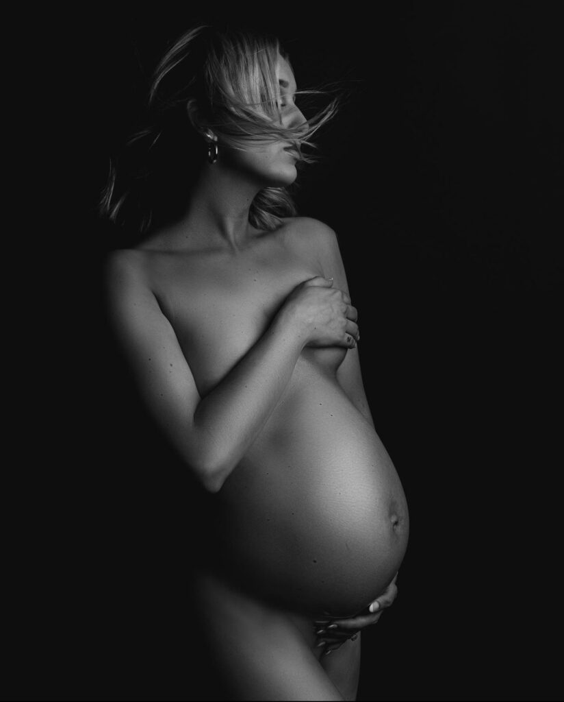 Black and white tasteful nude maternity photo done at a charlotte photography studio of mother with her hair in front of her face 