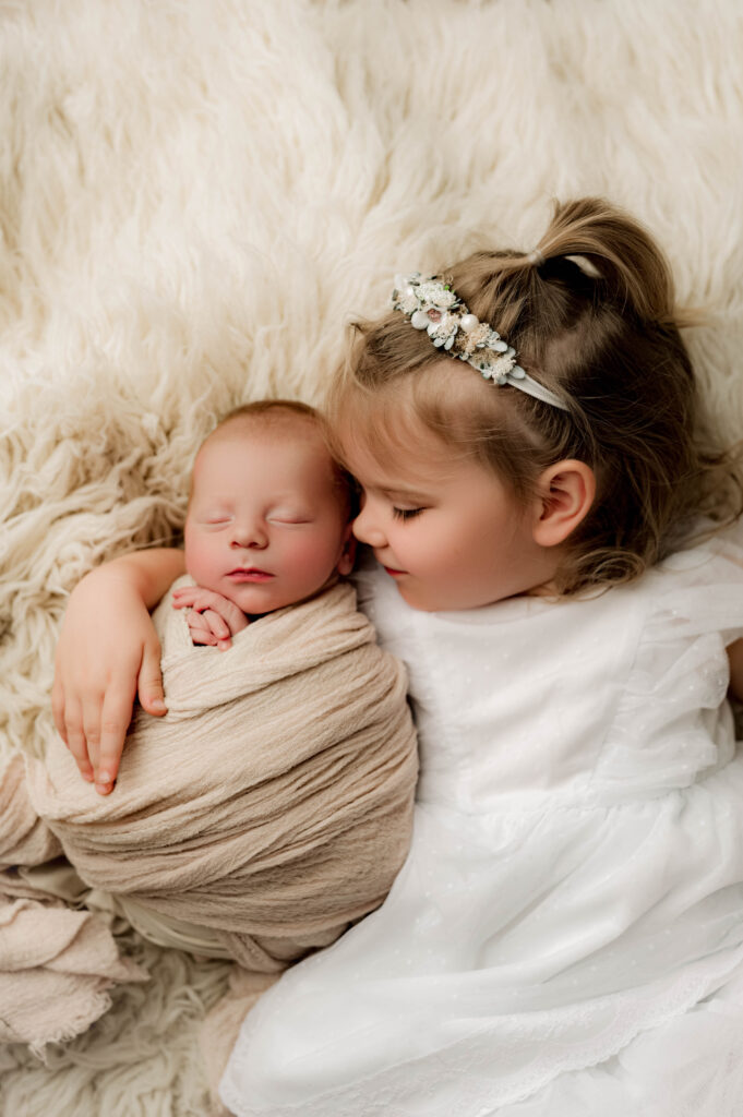 Little girl with her arms wrapped around her newborn brother looking down at him with her eyes closed