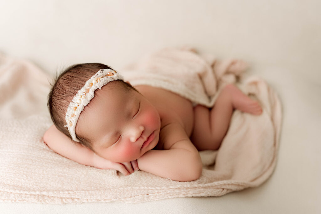 Newborn photo of baby girl with her chin on her hands facing the photographer.