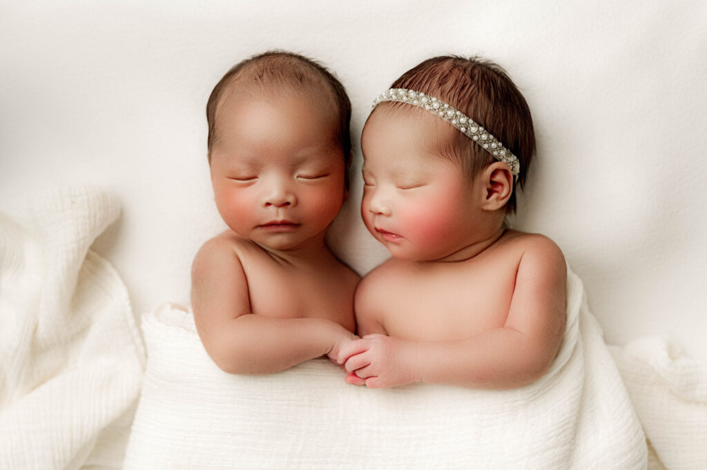 Twin newborns during their photography session holding hands while Maani looks at her brother.