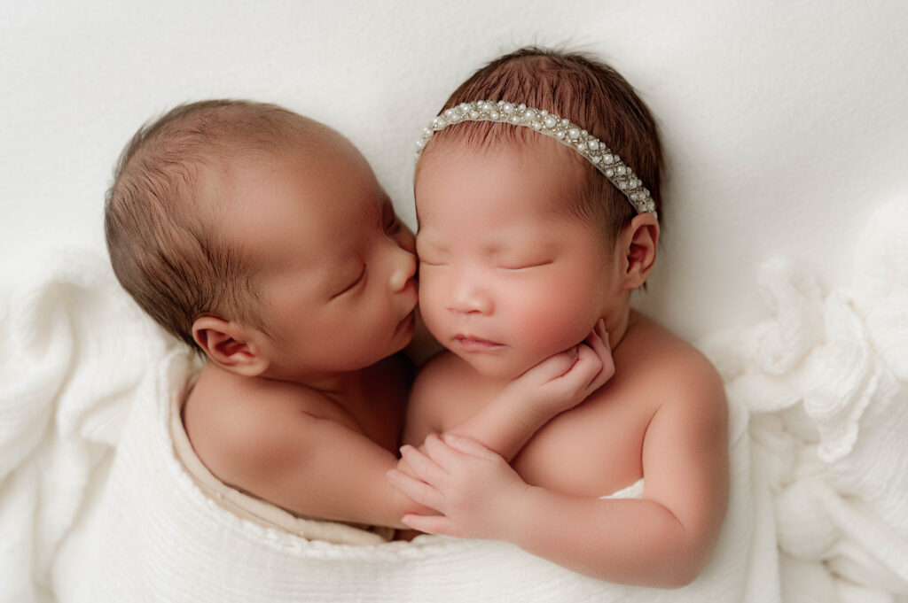 Newborn twins with the brother kissing his sister on the cheek during their newborn session.