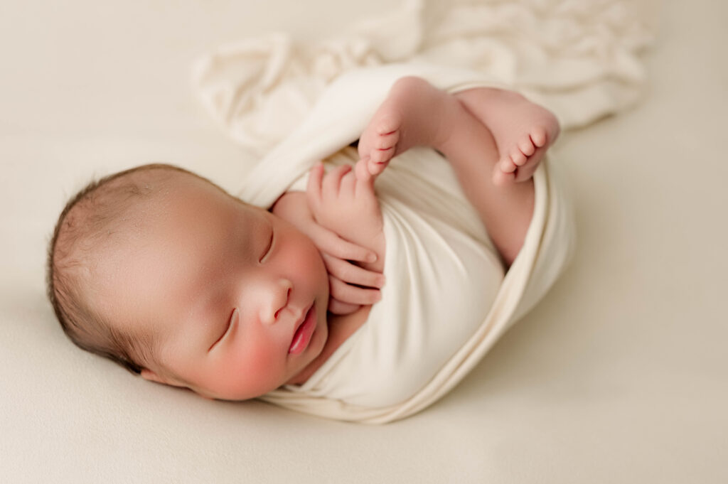 Newborn photo of baby boy wrapped looking towards photographer.