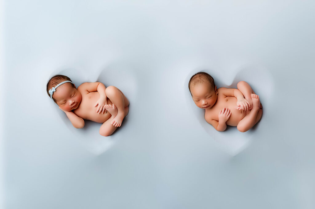 Newborn Boy/Girl twins inside hearts with a blue backdrop.