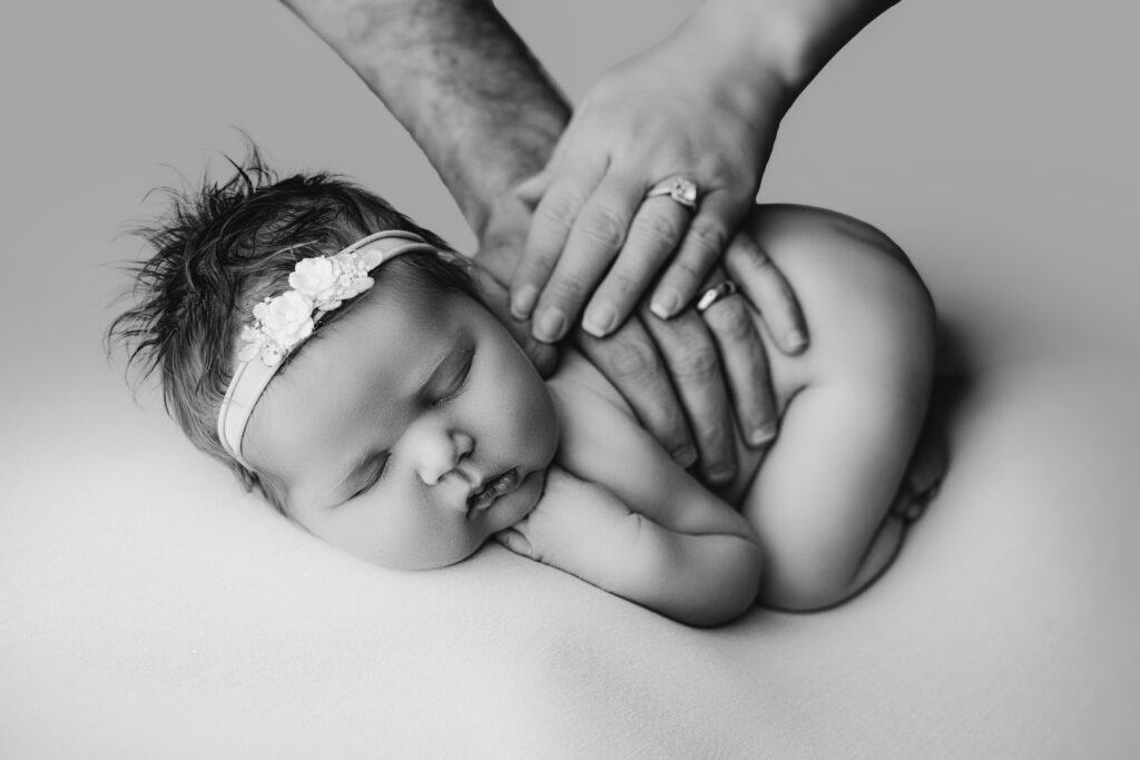 Baby girl curled up with her mom and dad's hands on her back posed during a charlotte newborn photography session.