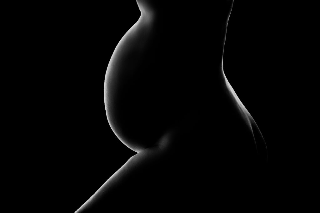 Black and white photo of pregnant mom's bump fully black expect for a small outline of white on her bump and back