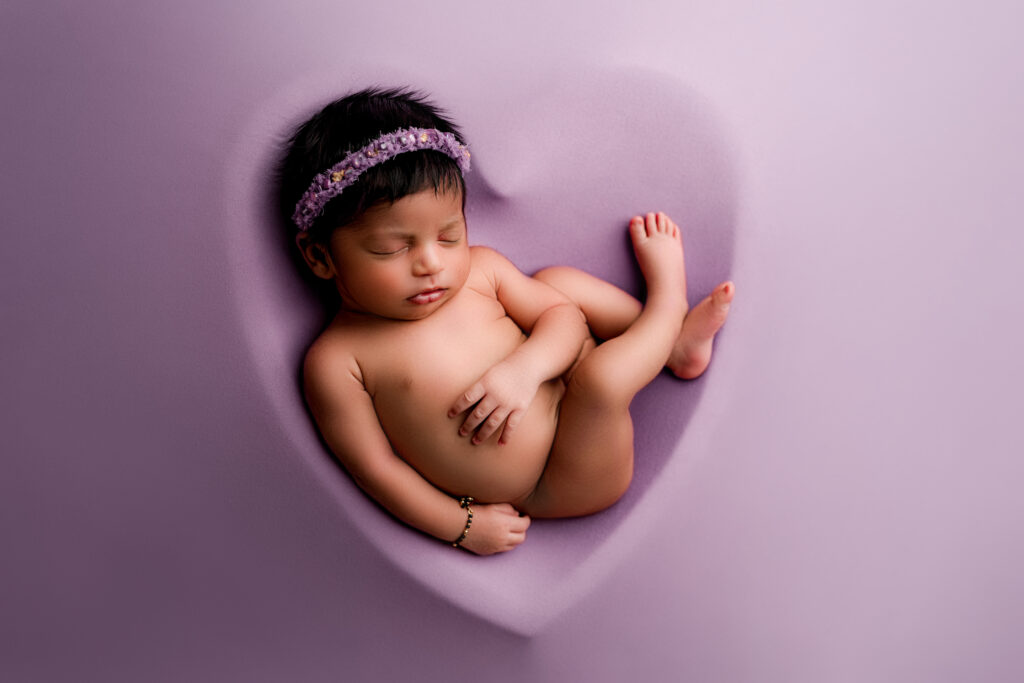 Baby girl in on purple background inside of heart bowl during her professional newborn photography session