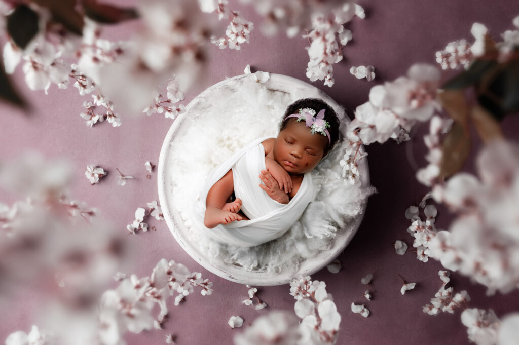 Baby girl laying in bowl with flowers surrounding her. 