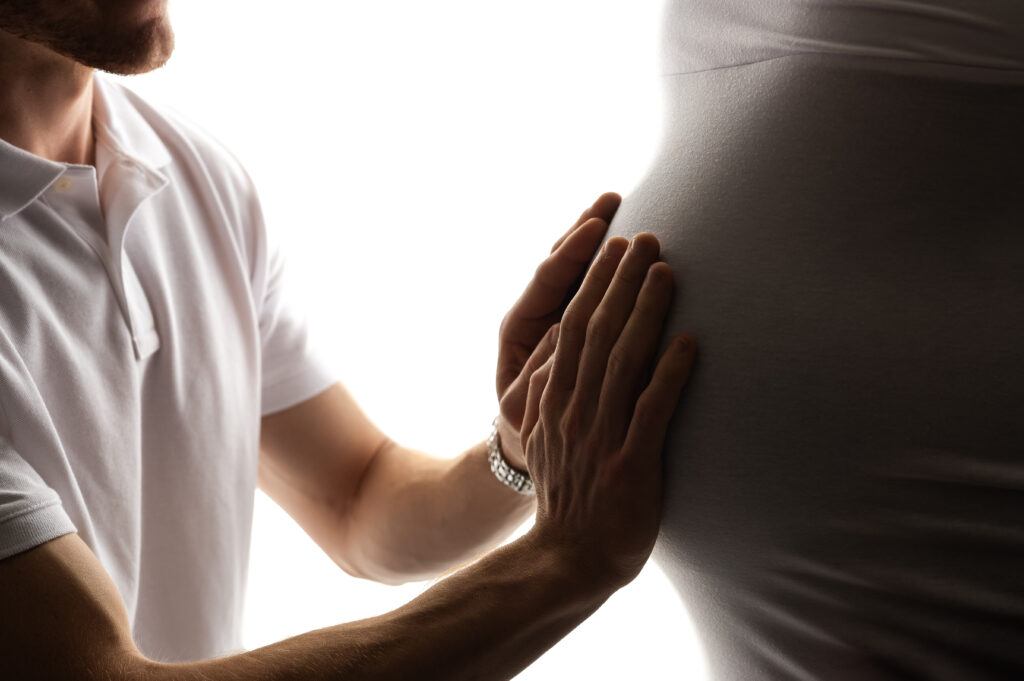 Close-up image of a man’s hands tenderly placed on a pregnant belly, symbolizing connection and anticipation in an intimate Charlotte maternity photography session at NicSo Studio.