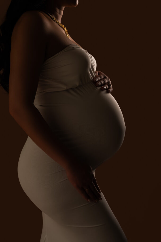 Close-up of baby bump cradled by mother’s hands in white gown during her luxury maternity photography session taken in Charlotte, NC