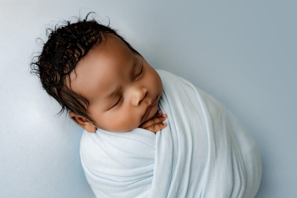 Newborn wrapped in blue blanket with knit wings framing head—serene studio image for Charlotte parents.