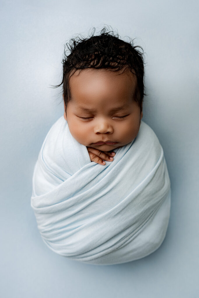 op-down view of baby cocooned in blue wrap, peaceful newborn portrait taken in Charlotte, NC.