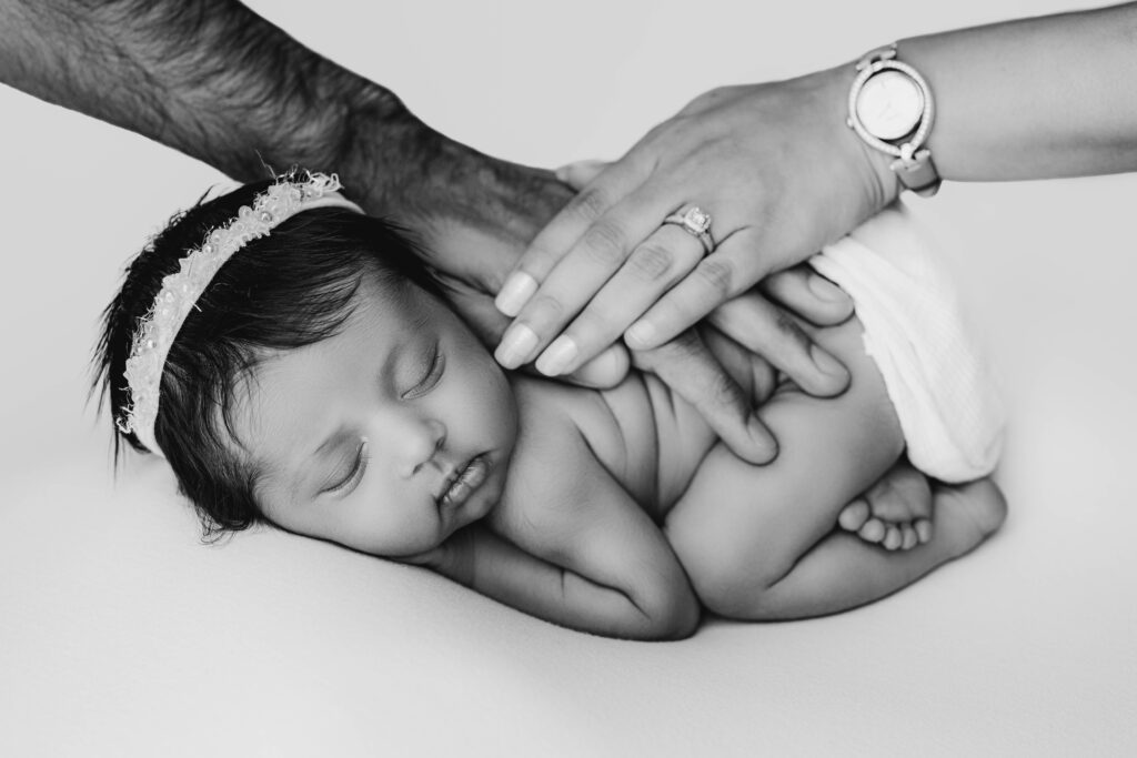 Black and white image of parents’ hands resting on sleeping newborn baby girl at NicSo Studio in Charlotte, NC