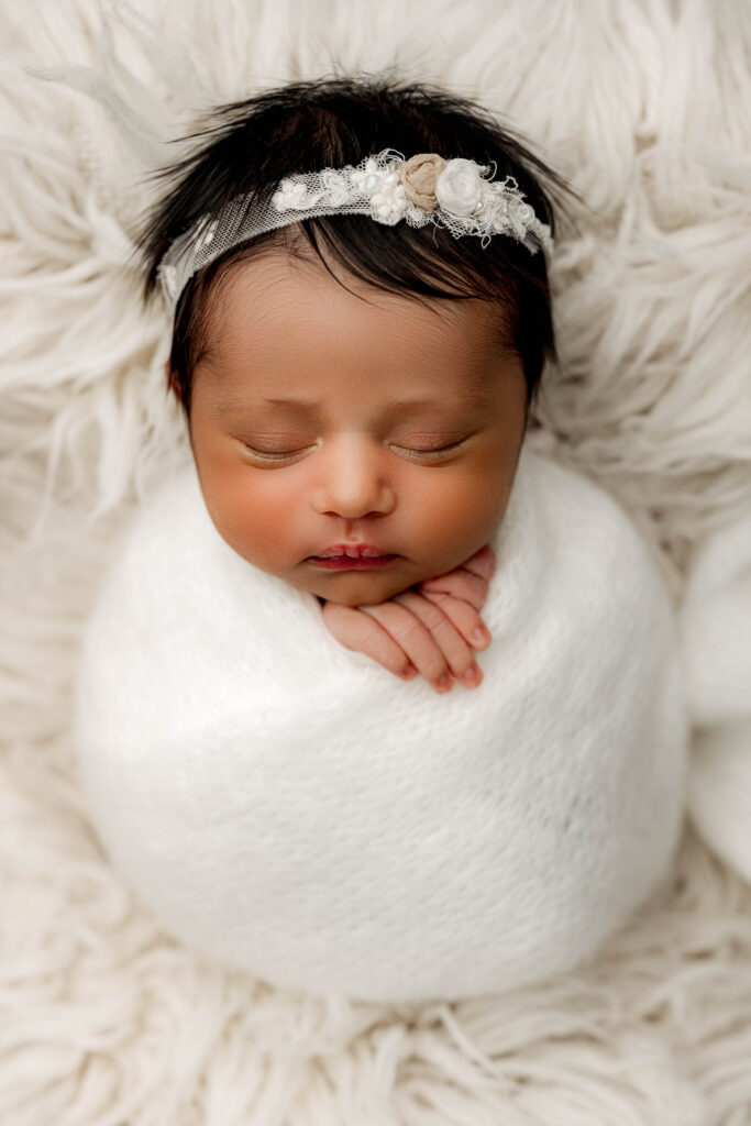 Swaddled newborn baby girl peacefully sleeping on white fur during rainbow baby photo session at NicSo Studio in Charlotte