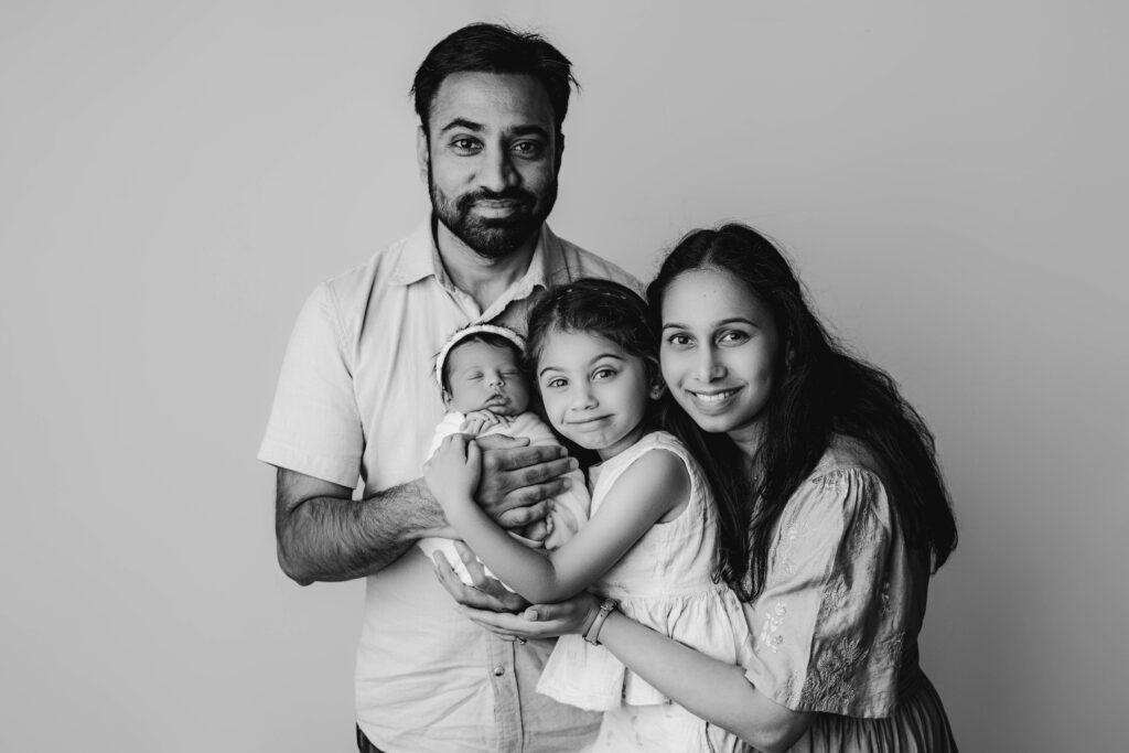 Family portrait with parents, big sister, and newborn rainbow baby girl looking straight at the camera in Charlotte photography studio