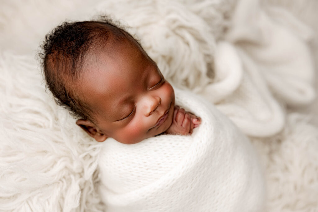 Premature newborn baby wrapped in a soft white knit blanket during a Charlotte newborn photography session at NicSo Studio, peacefully sleeping with a soft smile on a fluffy cream backdrop.