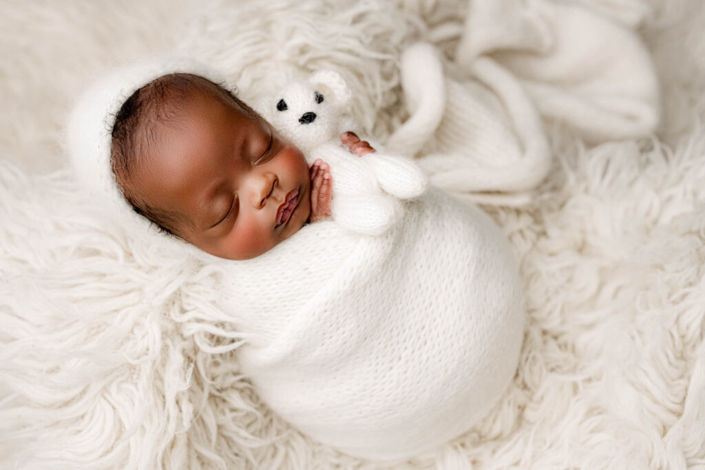 Preemie baby wrapped in white knit layers holding a tiny plush bear, photographed in a serene, neutral setup at NicSo Studio, Charlotte’s luxury newborn photography studio.