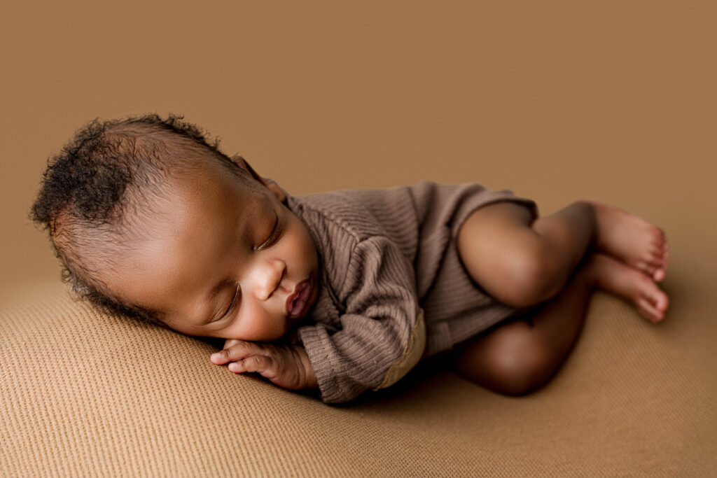 Close-up of a premature newborn curled on a tan backdrop in a brown knit romper, showcasing delicate features during a Charlotte luxury newborn portrait session