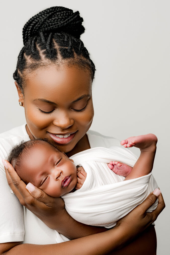 Mother holding her premature newborn close, both dressed in soft white tones, photographed during a heartfelt newborn session.