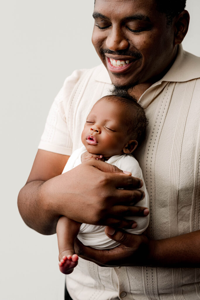 Father holding his premature newborn baby in a minimalist studio setting, captured during an intimate Charlotte newborn photography session