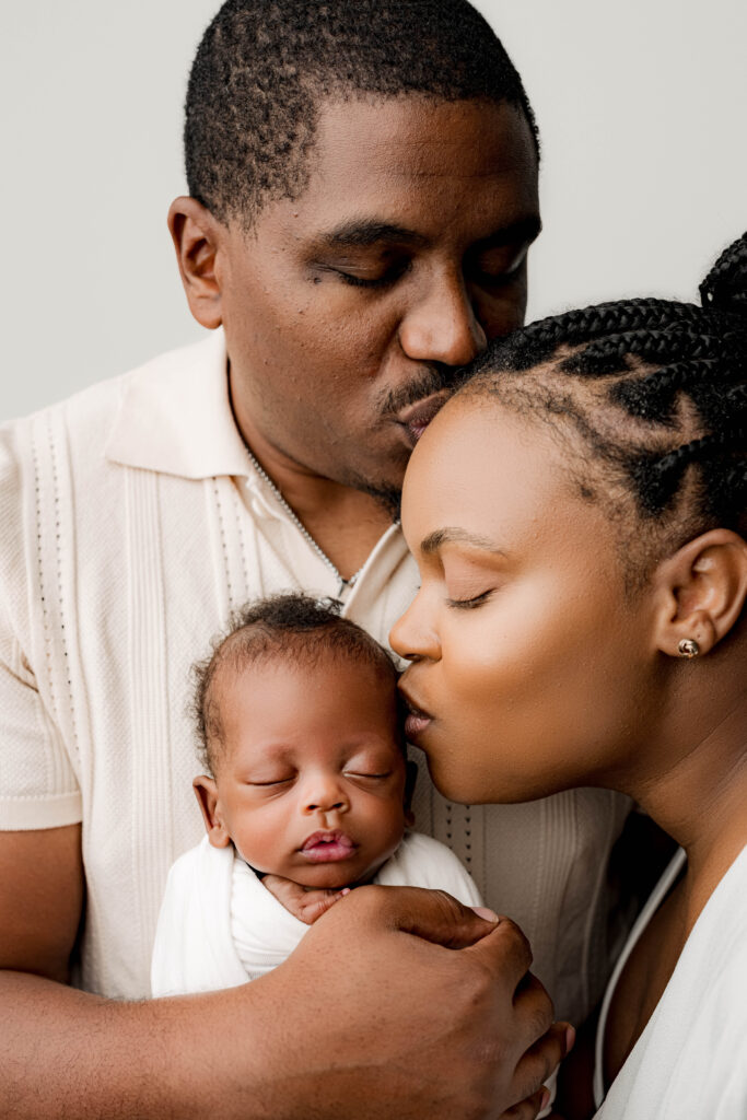 Parents embracing their premature newborn in a tender family portrait, mother and father kissing baby gently during a Charlotte newborn session at NicSo Studio.