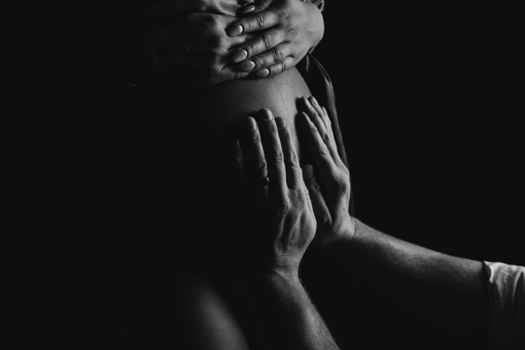  Black and white close-up of a couple's hands gently cradling a pregnant belly during a Charlotte studio maternity photography session