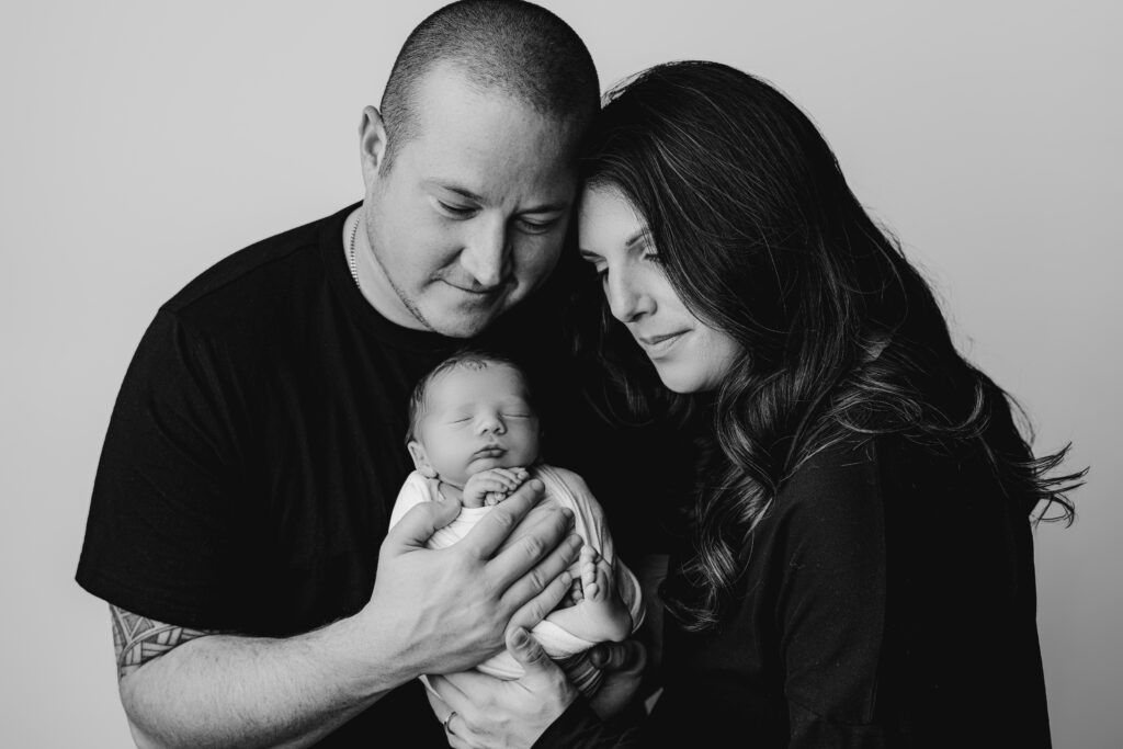 Black and white portrait of a mother and father gazing down at their newborn son during a studio newborn session.