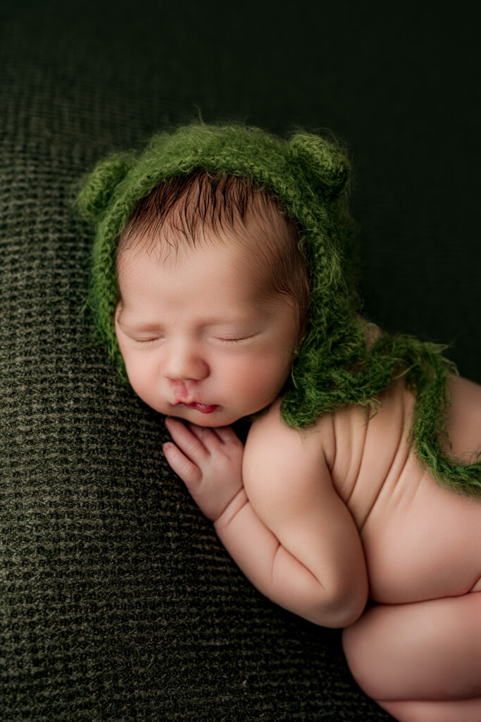 Newborn baby boy sleeping in a forest green bonnet on a textured green backdrop during a studio newborn session at NicSo Studio, Charlotte NC