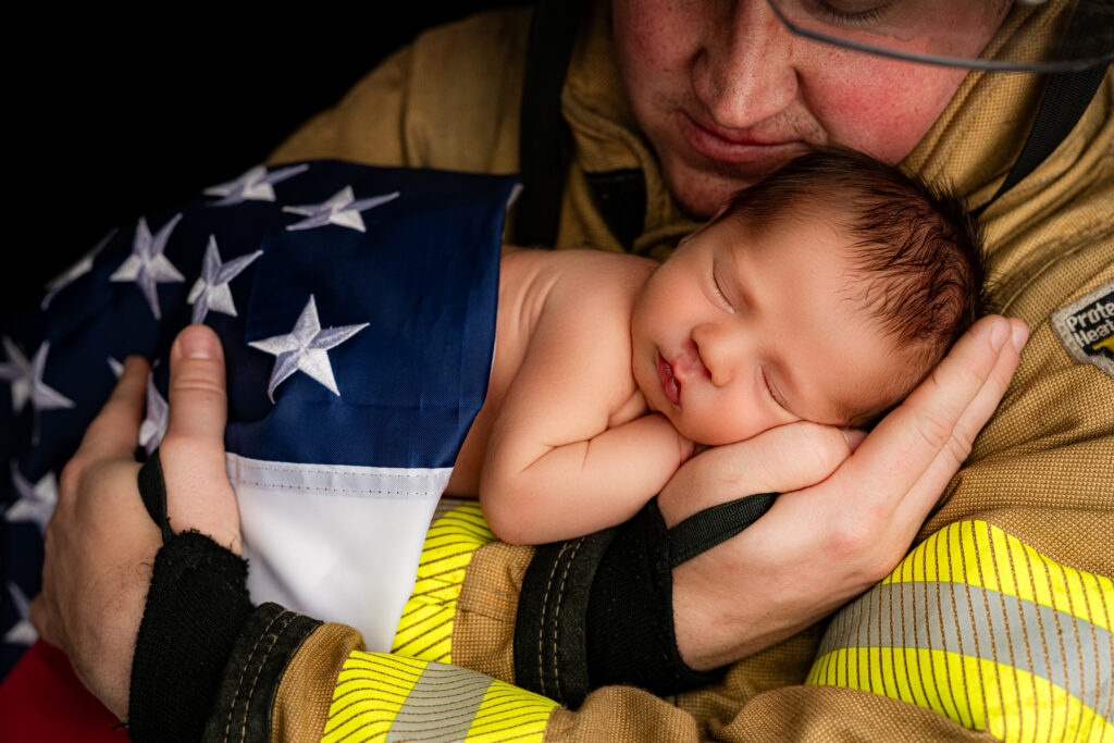 Newborn baby boy resting peacefully on an American flag in his firefighter father's arms during an emotional studio newborn session at NicSo Studio in Waxhaw, NC