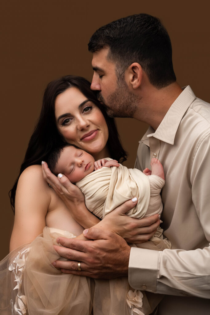 New parents holding their sleeping swaddled newborn together during a Charlotte newborn session at NicSo Studio, showing the continuity between sessions