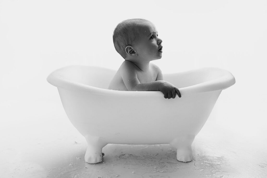 Black and white portrait of one year old baby boy in clawfoot tub after cake smash splash bath at NicSo Studio in Waxhaw NC