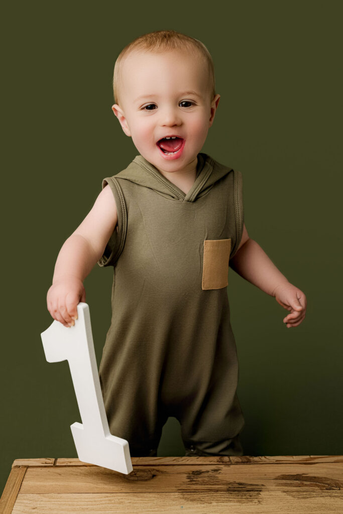 One year old baby boy holding number one sign during milestone session at NicSo Studio in Waxhaw NC