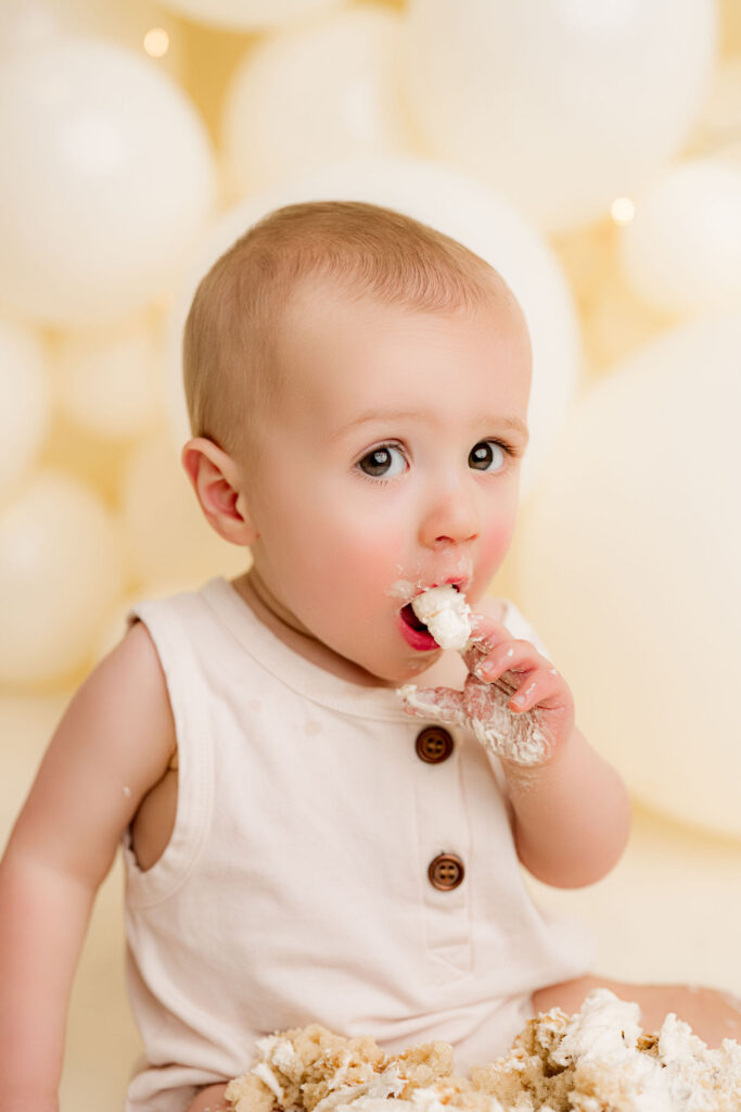 One year old baby boy eating birthday cake during cake smash session at NicSo Studio near Charlotte NC