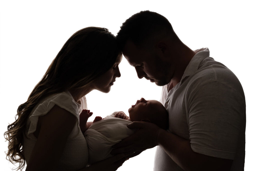 Newborn silhouette portrait of mom and dad holding sleeping baby at NicSo Studio in Waxhaw NC